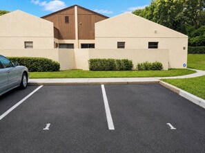 A parking lot with two white lines, a car, and a building with a brown roof and beige walls.