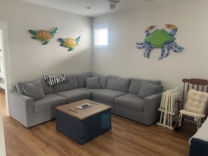 A living room with a grey sectional sofa, a wooden coffee table, and a small white chair. There are two wall decorations, one of a turtle and one of a crab. - On the Intracoastal Waterway with a dock. Bring your boat, minutes to the beach (Oak Island)