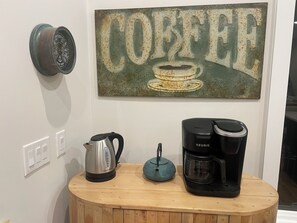 Une machine à café, une bouilloire et une œuvre d’art sur le thème du café, le tout posé sur une table en bois.
