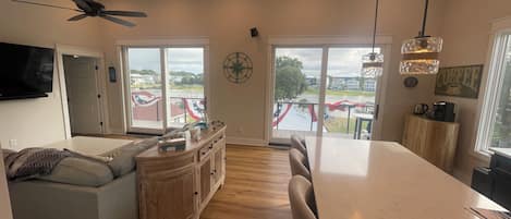 A spacious living area with a large window, a ceiling fan, and a dining area with a view of the outside.