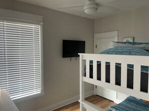 A bedroom with a bunk bed, a ceiling fan, a TV on the wall, and a window with blinds. - On the Intracoastal Waterway with a dock. Bring your boat, minutes to the beach (Oak Island)