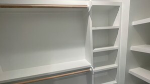 Huoneen nurkka, jossa on valkoiset seinät ja puulattia. Nurkassa on valkoisia hyllyjä, jotka ovat tyhjillään.