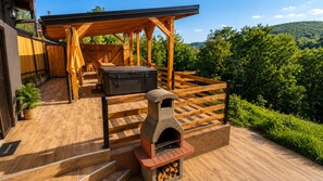 Une terrasse en bois avec un four en pierre, un barbecue et un espace salon couvert.