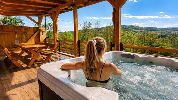 Ein Whirlpool mit Holzterrasse und Blick auf eine bewaldete Landschaft.