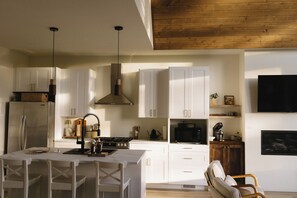 A modern kitchen with white cabinets, a central island, and a wooden ceiling. - The Vella | Private Modern Carriage House Near Shuswap Lake (Tappen)