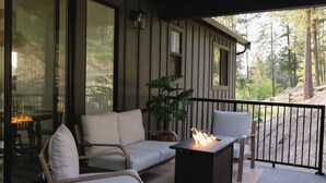 Ein überdachter Außenbereich mit einer Couch und Sesseln, einem Tisch mit Feuerstelle und Blick auf ein bewaldetes Gebiet.