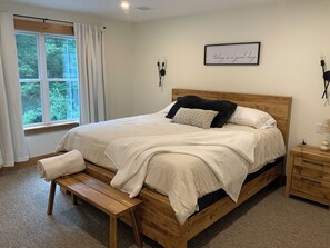 A bedroom with a wooden bed, a bench, a nightstand, and a window with curtains. - Ember and Oak (Richfield)