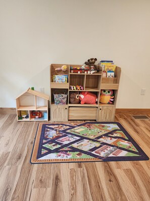 A wooden bookshelf with children's books and toys, a small dollhouse, and a colorful patchwork rug. - Ember and Oak (Richfield)