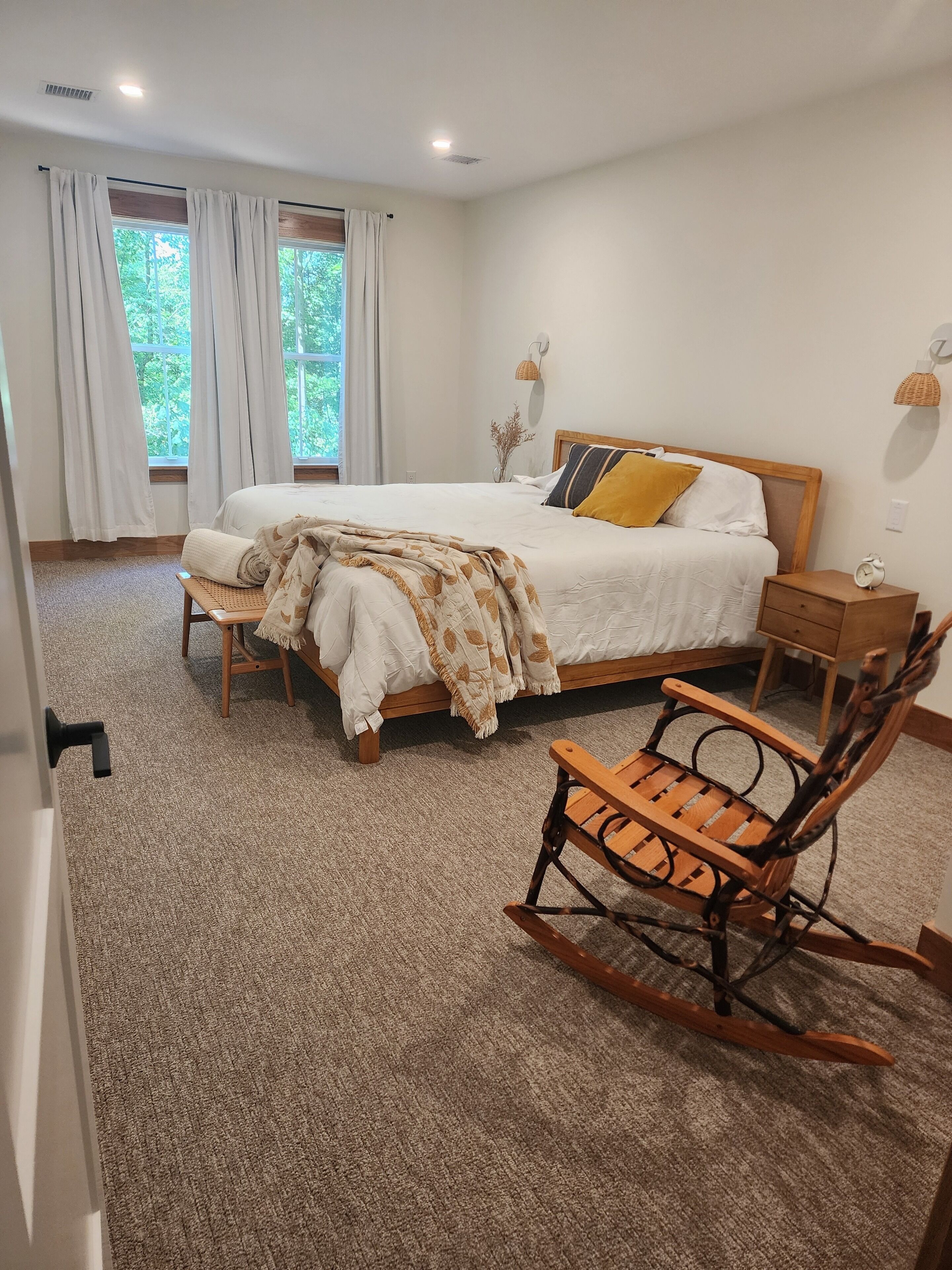A bedroom with a bed, bedside tables, a rocking chair, and a window with curtains.
