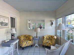 Ein Zimmer mit zwei gelben, floralen Ohrensesseln, einem weißen Tisch mit einer Lampe, einem gerahmten Bild und einem Fenster mit Blick nach draußen.
