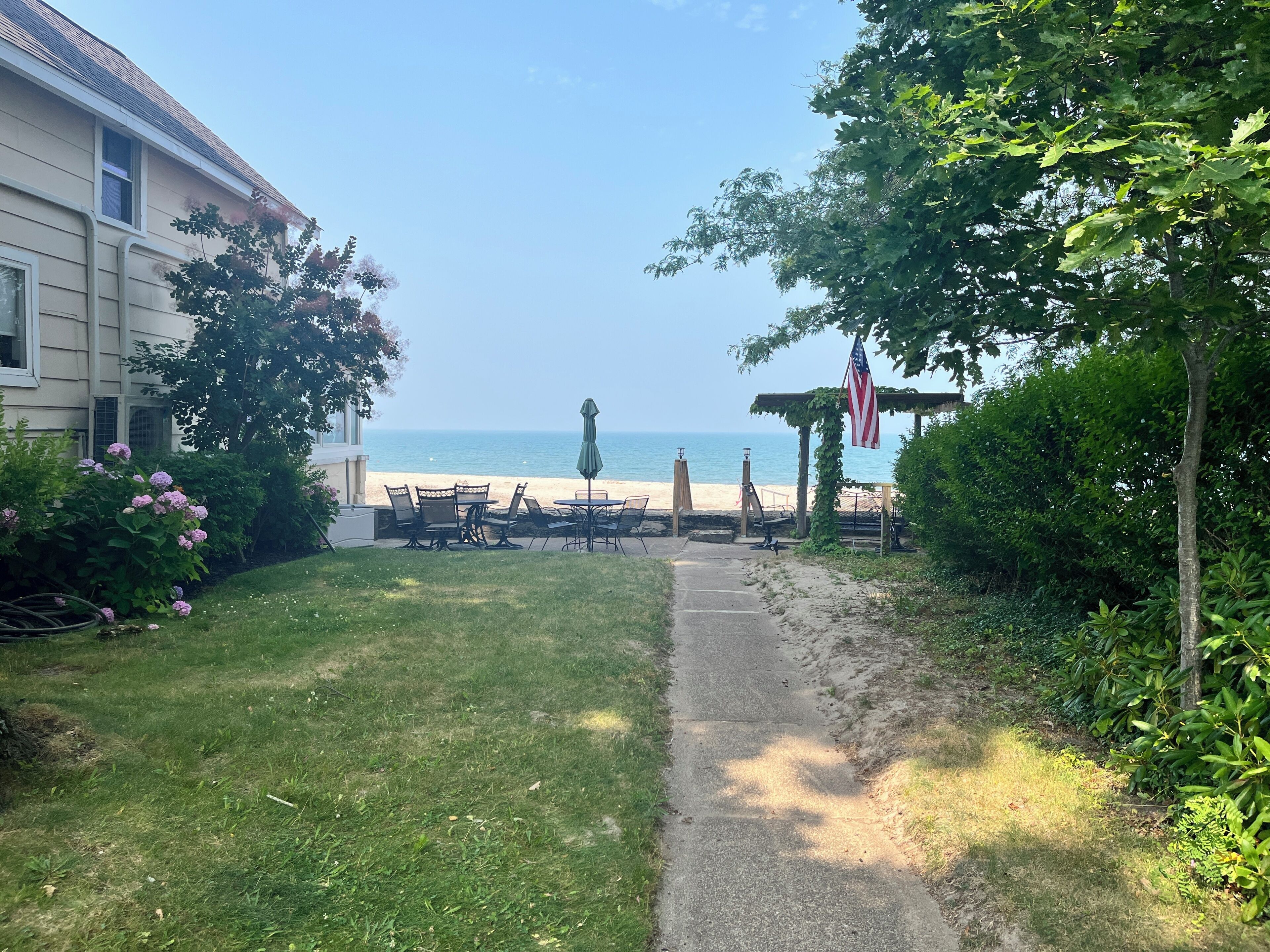 Een pad dat naar een strand leidt, met terrasmeubilair en een Amerikaanse vlag.