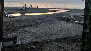 Uma praia com pôr do sol, um píer e algumas pessoas.