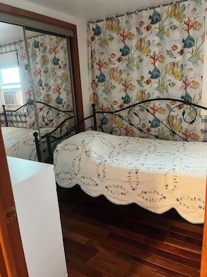 Ein Schlafzimmer mit einem Bett, Holzboden, einem Spiegel und einem Fenster mit Vorhängen.