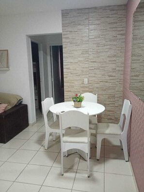 A dining area with a round table and four chairs, a small potted plant on the table, and a textured wall behind. - Well-located apartment near beaches, shopping, etc. (Vila Velha)