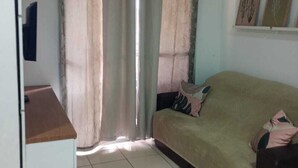 A room with a ceiling fan, a sofa, a small table, and curtains. - Well-located apartment near beaches, shopping, etc. (Vila Velha)