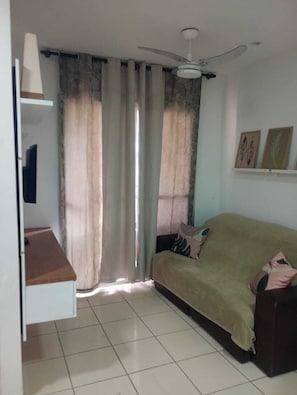 Ein Zimmer mit Deckenventilator, einer Couch, einem kleinen Tisch und Vorhängen.