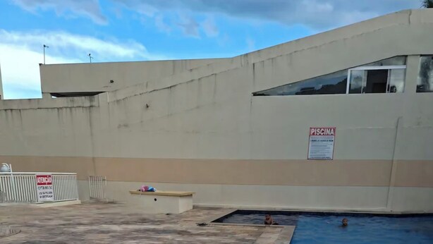 A swimming pool with a tiled deck and a 'PISCINA' sign, surrounded by a concrete wall. - Well-located apartment near beaches, shopping, etc. (Vila Velha)