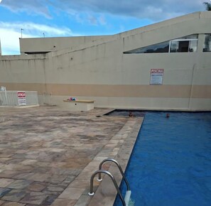 Een zwembad met betegeld zonnedek en een 'PISCINA' bord, omringd door een betonnen muur.