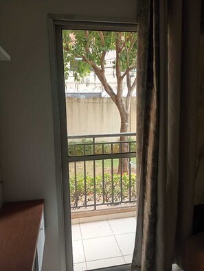Ein Zimmer mit einer Schiebetür, die auf einen Balkon mit Metallgeländer und einem Baum führt.