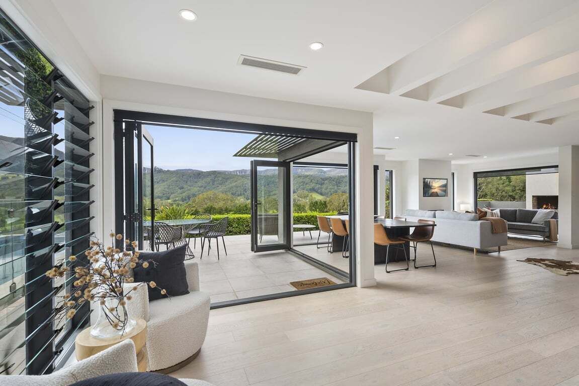 A modern interior with a dining area, kitchen, and a large sliding glass door leading to a balcony with a scenic view.