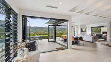 A modern interior with a dining area, kitchen, and a large sliding glass door leading to a balcony with a scenic view.