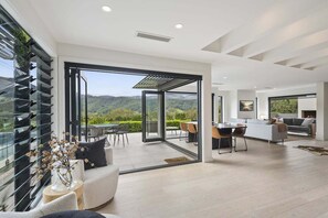A modern interior with a dining area, kitchen, and a large sliding glass door leading to a balcony with a scenic view.