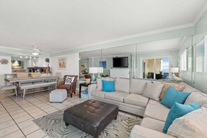 A spacious living area with a sofa, ottoman, and a dining table with chairs. - Fall Deals + Snowbird Rates | Gulf Front Beach Escape (Panama City)