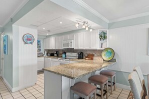 A kitchen with white cabinets, a granite countertop, a microwave, a coffee maker, and a decorative plate. - Fall Deals + Snowbird Rates | Gulf Front Beach Escape (Panama City)