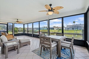 A sunroom with a view of a residential area, a ceiling fan, and a dining table with chairs. - Intracoastal Waterfront Home | Private Pool, Boat Dock, Screened Lanai, Sleeps 6 (Palm Coast)