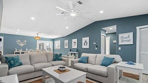 Ein Wohnzimmer mit zwei Sofas, einem Couchtisch, einem Beistelltisch, einem Deckenventilator und Wandbildern.