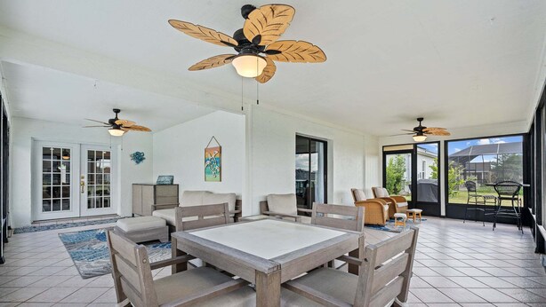 Eine überdachte Terrasse mit Esstisch und Stühlen, Deckenventilatoren und Blick ins Freie.