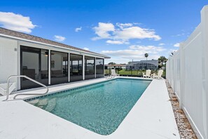 A swimming pool with a covered area, white walls, and a clear blue sky. - Intracoastal Waterfront Home | Private Pool, Boat Dock, Screened Lanai, Sleeps 6 (Palm Coast)