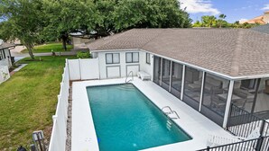 Ein rechteckiger Swimmingpool mit weißer Liegefläche, umgeben von einem weißen Zaun, und ein überdachter Patio-Bereich mit Blick auf den Garten.
