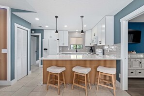 A modern kitchen with white cabinets, a central island with stools, and a built-in oven. - Intracoastal Waterfront Home | Private Pool, Boat Dock, Screened Lanai, Sleeps 6 (Palm Coast)