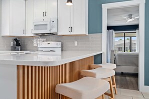 A modern kitchen with white cabinets, a microwave, and a stove. There are three bar stools with a wooden slatted design. - Intracoastal Waterfront Home | Private Pool, Boat Dock, Screened Lanai, Sleeps 6 (Palm Coast)