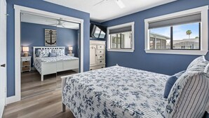 Ein Schlafzimmer mit Bett, Kommode, Nachttisch, Deckenventilator und einem Fenster mit Blick.