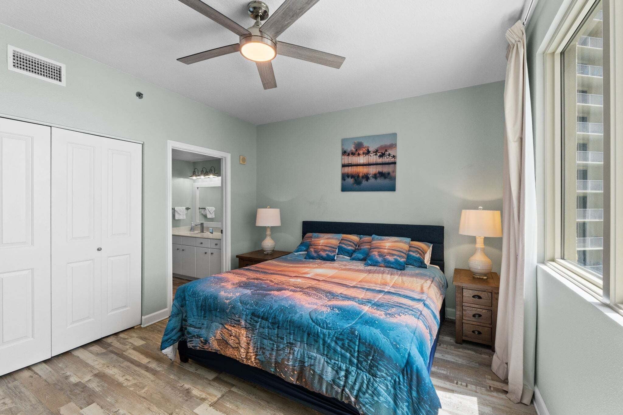 A bedroom with a bed, a ceiling fan, a window, and a bathroom with a mirror and sink.
