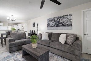 Ein Wohnzimmer mit Ecksofa, Couchtisch, einer Pflanze und einem großen abstrakten Gemälde an der Wand.