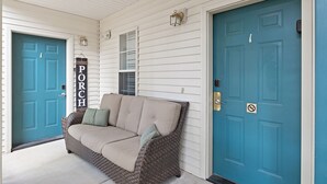 En veranda med en beige sofa, to døre og et skilt med teksten 'PORCH'.