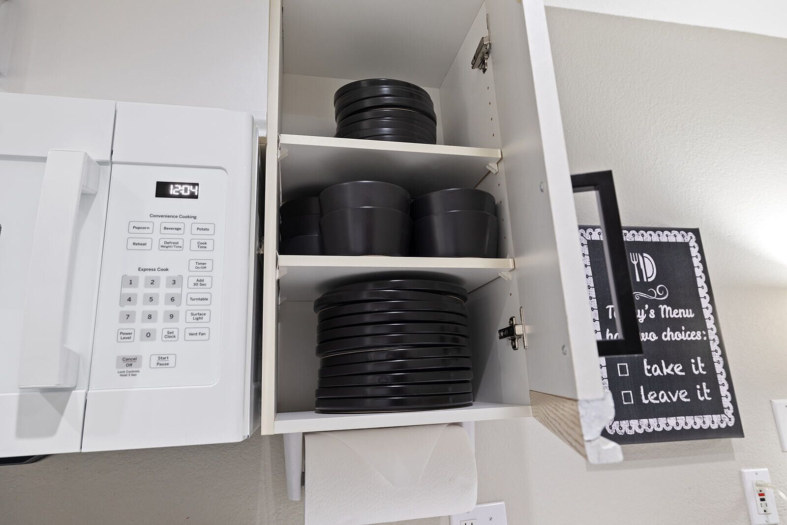 A kitchen with a microwave, black pots, and a chalkboard menu.