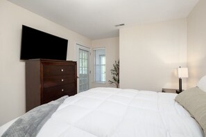 Une chambre à coucher avec un lit, une commode, une télévision, une fenêtre et une lampe de chevet.