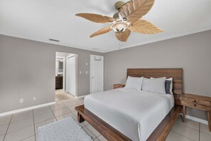 A bedroom with a bed, wooden headboard, nightstands, a ceiling fan, and a door leading to another room. - Kissimmee 4BR Poolside Retreat | Private Pool & Sauna (Kissimmee)