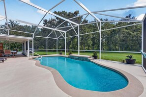 Ein Schwimmbad mit Glasveranda, umgeben von einer Terrasse mit Gartenmöbeln.