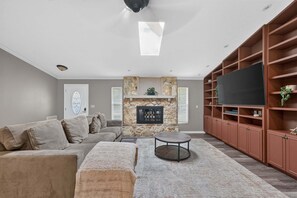 Ein Wohnzimmer mit einem Ecksofa, einem Kamin, einem Flachbildfernseher und eingebauten Regalen.