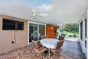 Eine überdachte Terrasse mit Tisch und Stühlen, einem Deckenventilator und Blick auf einen Garten.