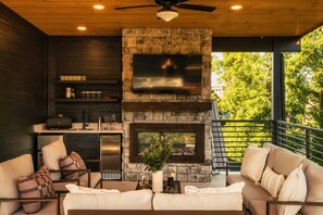 A modern living room with a stone fireplace, a flat-screen TV, and a balcony with a railing. - Golf Simulator/Rooftop Deck/Hot Tub/3BR/Sleeps 8! (Pigeon Forge)