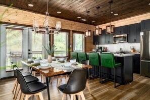 A modern kitchen with a wooden ceiling, a dining area with a wooden table and black chairs, and a bar area with green chairs. - Golf Simulator/Rooftop Deck/Hot Tub/3BR/Sleeps 8! (Pigeon Forge)