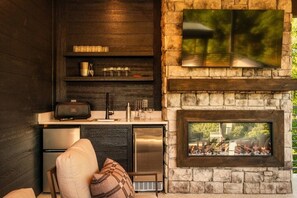 Een moderne keuken met een ingebouwde grill, een flatscreen televisie en een stenen openhaard.