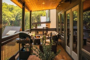Een overdekt terras buiten met een barbecue, zitgedeelte en grote ramen.