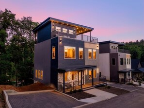 A modern two-story building with a balcony, large windows, and a driveway. - Golf Simulator/Rooftop Deck/Hot Tub/3BR/Sleeps 8! (Pigeon Forge)